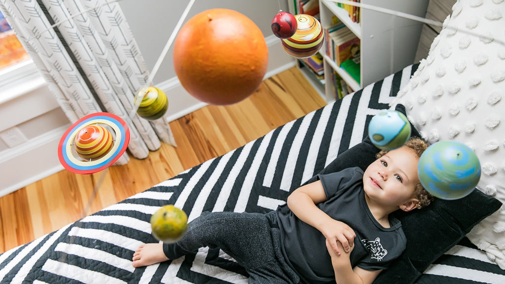 baby looking at toy planets from his bed